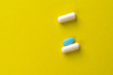 2 white pills and 1 blue tablet on a yellow background. medical background