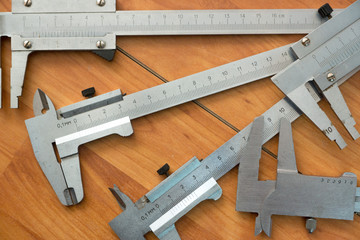 Close-up of several calipers lying on a wooden surface, some details are not in focus. Measuring...