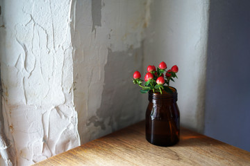 Red artificial flower in glass jar decorated on wooden table -Interior decoration