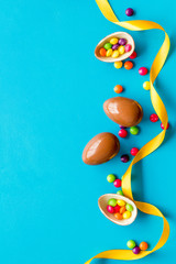 Easter background with chocolate eggs and dragees on blue background top-down frame copy space
