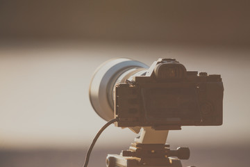 Camera DSLR set on tripod capturing sunset on beach.