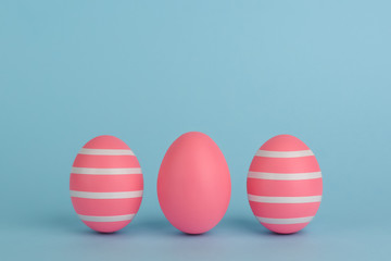  Three Easter decorated pink eggs. Striped pink eggs in a row on a blue background. White strips. Copy space. Pink monochrome Easter concept.