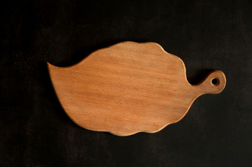 The kitchen composition. Beech cutting board in the shape of a leaf close-up on a dark concrete background.