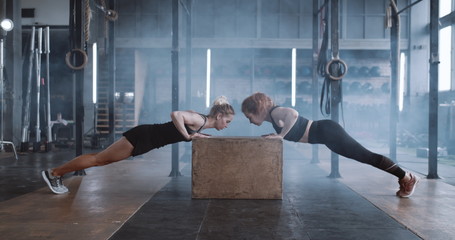Side view happy attractive young blonde woman working out with personal female coach in gym doing...