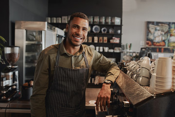 Portrait of young afro-american male business owner behind the counter of a coffee shop smiling looking at camera