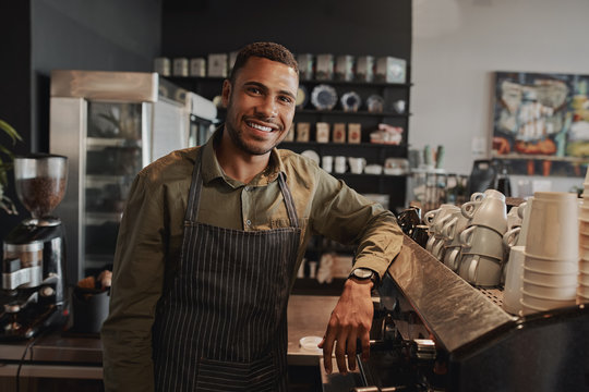 Portrait of young afro-american male business owner behind the counter of a coffee shop smiling looking at camera