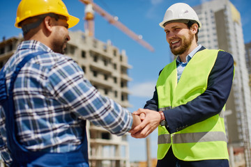 Two male engineers shake each others hands friendly.