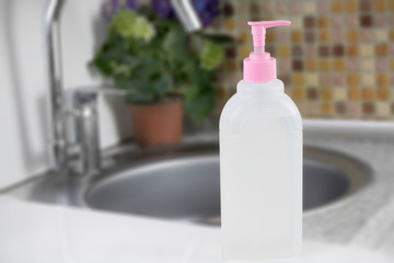 Fototapeta na wymiar The cleaning transparent gel-like product for washing hands and dishes in focus. Biodegradable plastic and environmentally friendly. Against the background of the sink and water tap, a white kitchen
