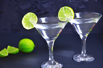 Two glasses of martini with lime on a black background. Two glasses of martini cocktail in a bar.