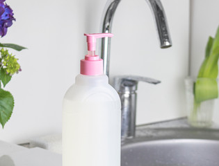 The cleaning transparent gel-like product for washing hands and dishes in focus. Biodegradable plastic and environmentally friendly. Against the background of the sink and water tap, a white kitchen