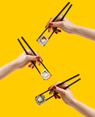 Women's hands hold sushi rolls with sticks. Yellow background. Creative concept