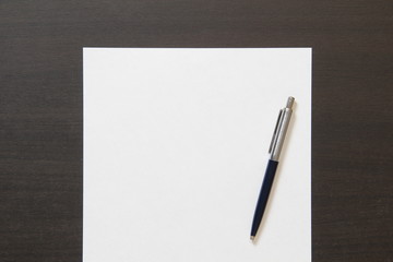 Template of white paper with pen on dark wenge color wooden background.
