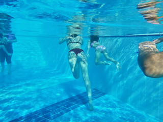 Bodies of mother and small daughter swimming in a pool under water. Woman and girl. Blue color