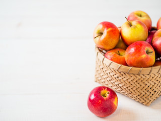 Apples harvest concept. Braided bamboo basket with red apples on white wooden background with copy space for text or design.