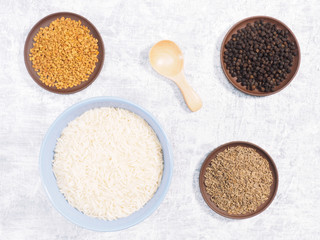 Indian long grain Basmati rice in blue ceramic bowl, black pepper, cumin (jeera), fenugreek on white concrete background