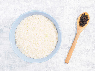 Indian long grain Basmati rice in blue ceramic bowl, black pepper in spoon on white concrete background