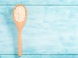 Basmati rice in wooden spoon vertically on blue wooden background