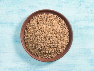 Spice cumin (jeera) in clay plate on blue wooden background