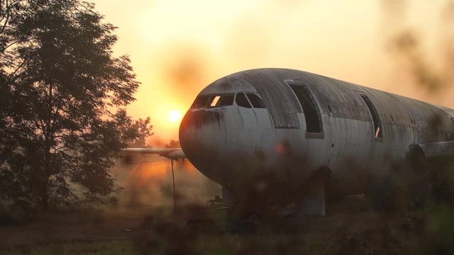 Abandoned airplane wreck behind vegetation, on a field in Thailand, during sunset