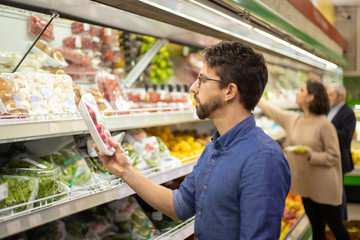 Man looking at vegetables in grocery store. Side view of men and woman holding shopping baskets and choosing fresh fruits and vegetables in supermarket. Shopping concept