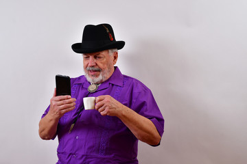 Fototapeta premium Happy old man using his smartphone and enjoing a cup of espresso.