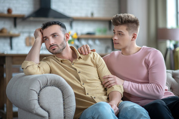 Man in orange shirt sitting on the sofa feeling upset and offended