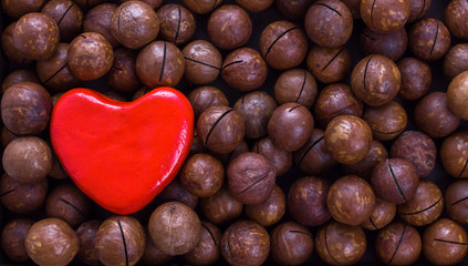 Red heart on a background of macadamia nuts. The concept of a healthy diet, the prevention of heart disease. Flat lay, copy space.