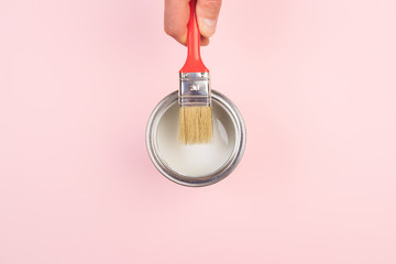 hand holding Brush  on open can of white paint on pastel pink background. Renovation concept - Image