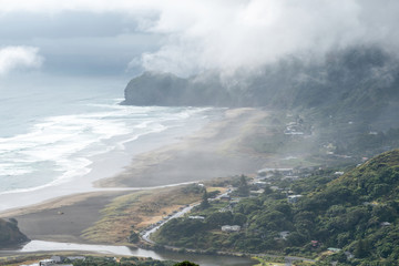 Aerial view of North Piha beach with sand dunes and Piha village houses covered in thick fog