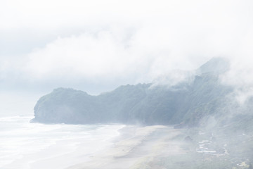 Aerial view of Te Waha Point and Kohunui Bay at North Piha beach covered in thick fog