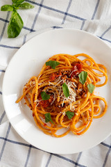Homemade Bucatini all Amatriciana Pasta in a white plate on cloth, top view. Flat lay, overhead, from above.