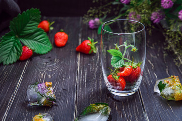 The berries of ripe large strawberries lie in a clear glass and on a wooden table