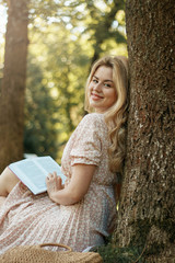 Young blonde woman in summer park reads book, vertical photo