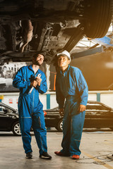 Mechanic in blue work wear uniform inspects the car bottom with a wrench with his assistant....