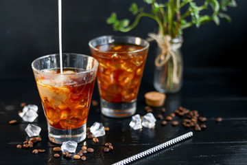 Iced coffee in a tall glass with milk and pieces of ice. On a dark background.