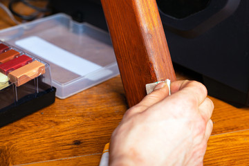 master wipes a scratch on a leg  from wooden furniture restoration repair close-up