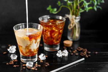 Iced coffee in a tall glass with milk and pieces of ice. On a dark background.