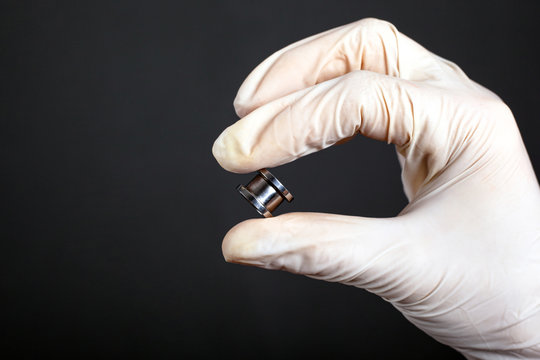 hand in a white disposable glove holds a piercing tunnel on a dark background ear jewelry close-up