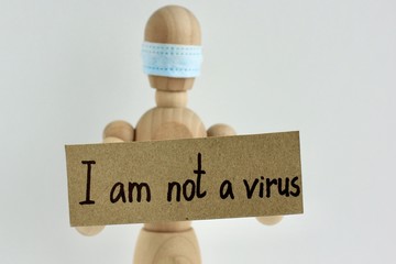 Cardboard sign with text I am not a virus in the hands of a wooden doll or mannequin in a medical mask. Concept of anti racism, anti xenophobia, the social situation around the Coronavirus or Covid-19