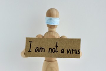 Cardboard sign with text I am not a virus in the hands of a wooden doll or mannequin in a medical mask. Concept of anti racism, anti xenophobia, the social situation around the Coronavirus or Covid-19
