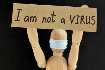 Cardboard sign with text I am not a virus in the hands of a wooden doll or mannequin in a medical mask. Concept of anti racism, anti xenophobia, the social situation around the Coronavirus or Covid-19