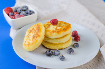 Pancakes with strawberries, raspberries, blueberries on a blue background.