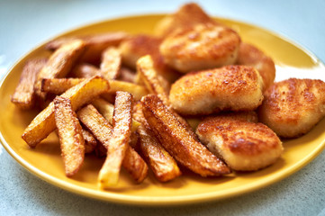 Tasty homemade potato french fries with chiken nuggets on yellow dish