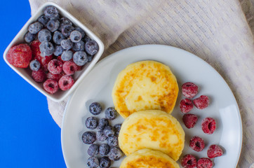 Pancakes with strawberries, raspberries, blueberries on a blue background.