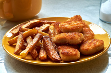 Tasty homemade potato french fries with chiken nuggets on yellow dish