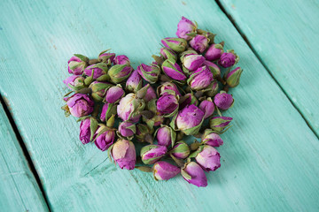 heart made dried rose buds on turquoise wooden surface