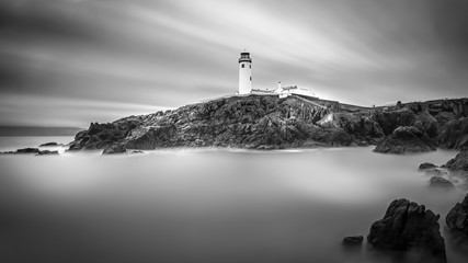 Twilight yields to dawn at Fanad Head Lighthouse. Smudges of clouds and misty water. Black and white long exposure photography with selective focus. Wild Atlantic Way, Donegal, Ireland