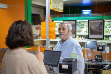 Man and woman talking at pay desk in supermarket. Customer talking with cahier while buying goods in grocery store. Shopping concept