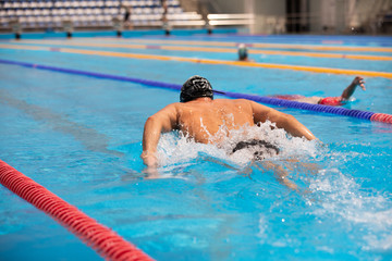 Athletic man swimming in butterfly style in the swimming pool with clear blue water.