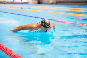 Athletic man swimming in butterfly style in the swimming pool with clear blue water.